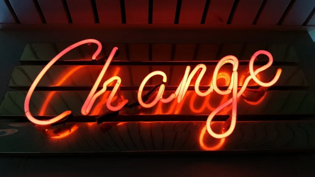 The image-60 features a neon sign displaying the word "Change" in vibrant red and orange hues. Set against a dark backdrop with wooden slats, the brightly illuminated cursive letters create a warm and inviting atmosphere.
