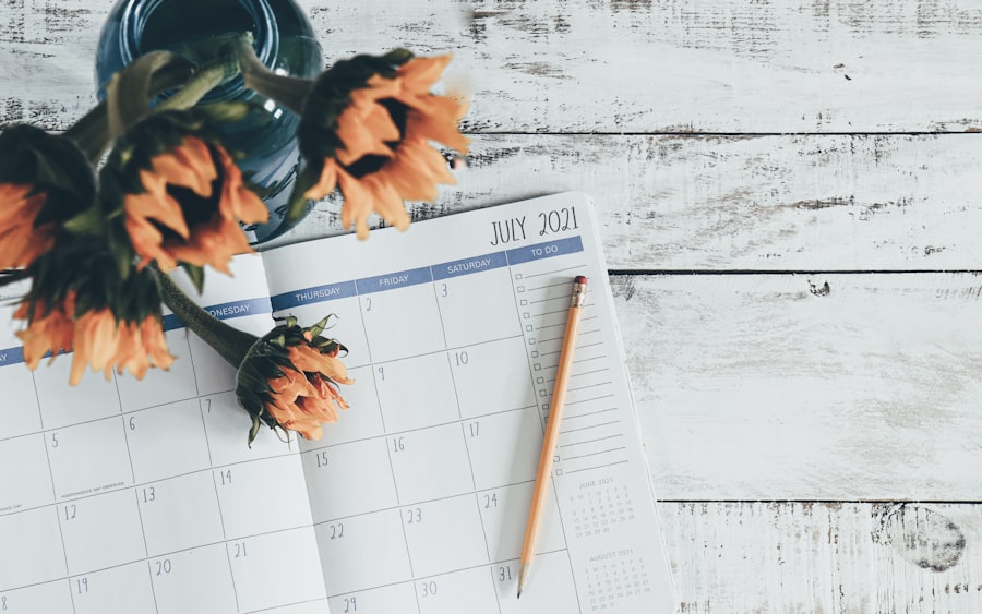 An open July 2021 calendar on a white wooden surface, paired with an orange pencil. Sunflowers in a blue vase partially grace the scene, enhancing the ambiance. (image-1).