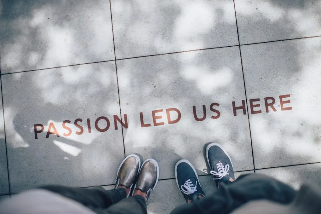 Feet in metallic shoes and blue sneakers stand on a pavement with "PASSION LED US HERE" in bold letters, while tree leaf shadows cast gently around. This moment is captured in image-2.
