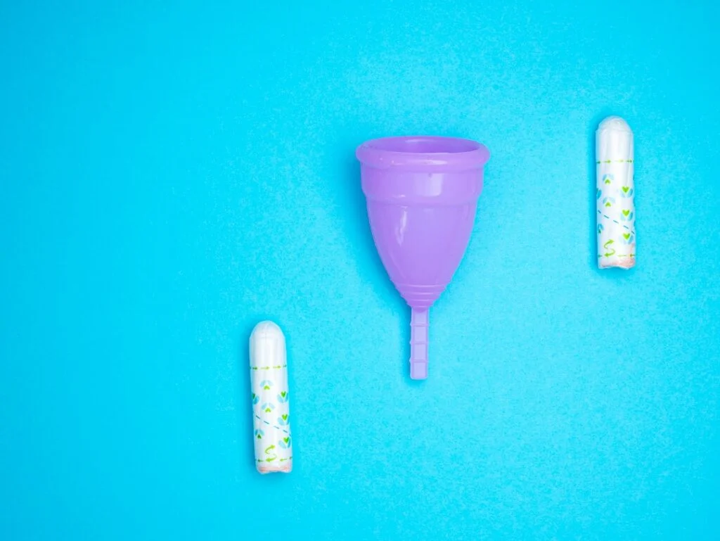 On a bright blue background, image-4 shows a purple menstrual cup positioned between two wrapped tampons.