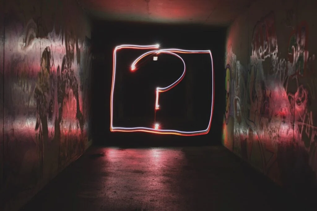 The image showcases a dark graffiti-covered tunnel illuminated by a bright light painting of a large question mark framed by a rectangle, creating a mysterious and intriguing atmosphere.