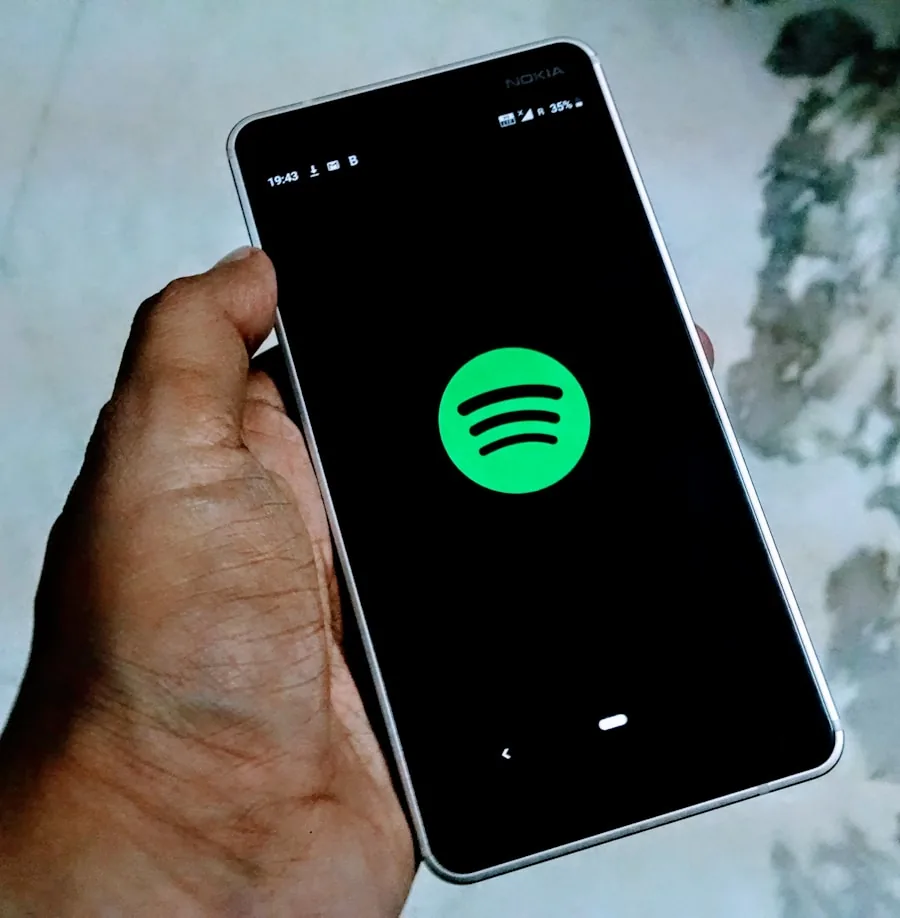 A hand is holding a smartphone displaying the Spotify app logo on its screen. The phone is identified as image-4, and the background is blurred.