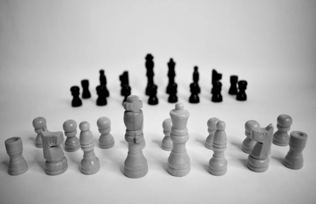 Image-3: Black and white photo of a chessboard with light pieces in the front and dark pieces behind, all set up on a plain surface, ready for play.