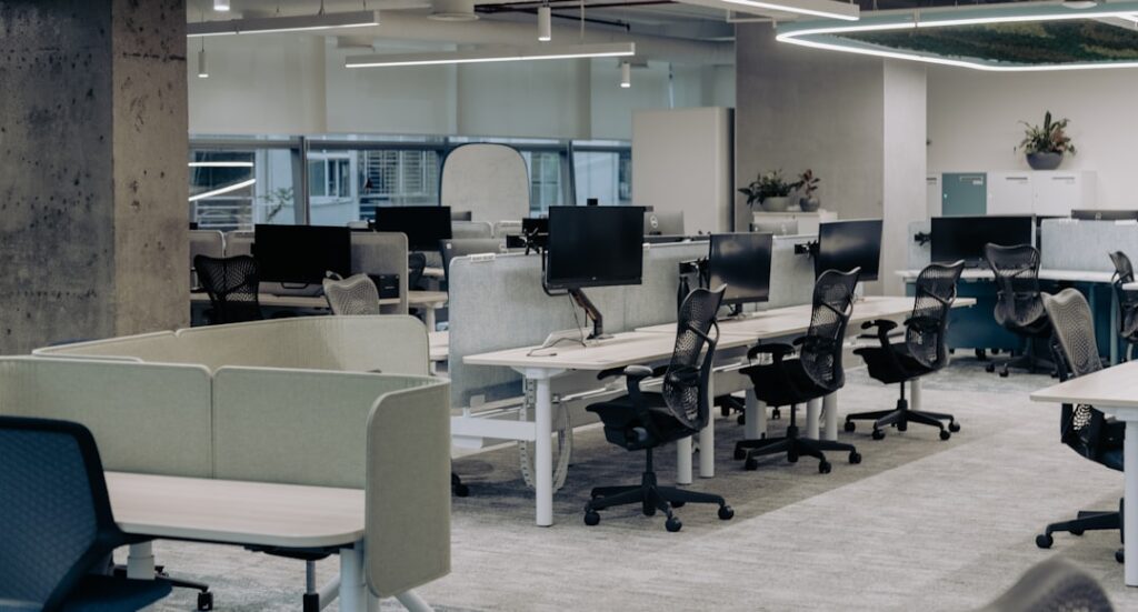 The image "image-2" shows a modern open-plan office with empty desks, black chairs, monitors, and partition dividers. Large windows fill the space with natural light, creating a bright and spacious work environment.