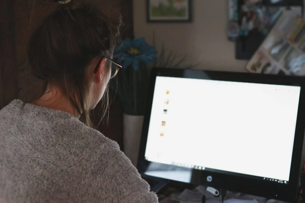 The product image-6 shows a person with long brown hair, glasses, and a gray sweater sitting at a desk working on a computer. The workspace features papers, a keyboard, and a vase of blue flowers.