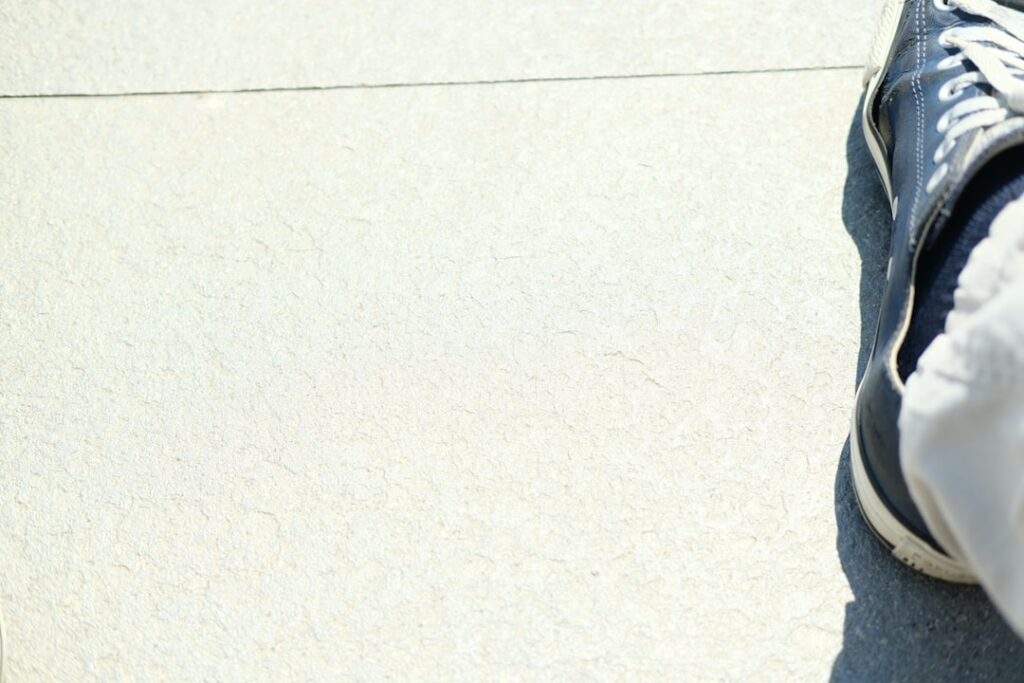 A person in light-colored pants and blue sneakers sits on a pale, textured concrete surface at the right of the image. The background is mostly empty.