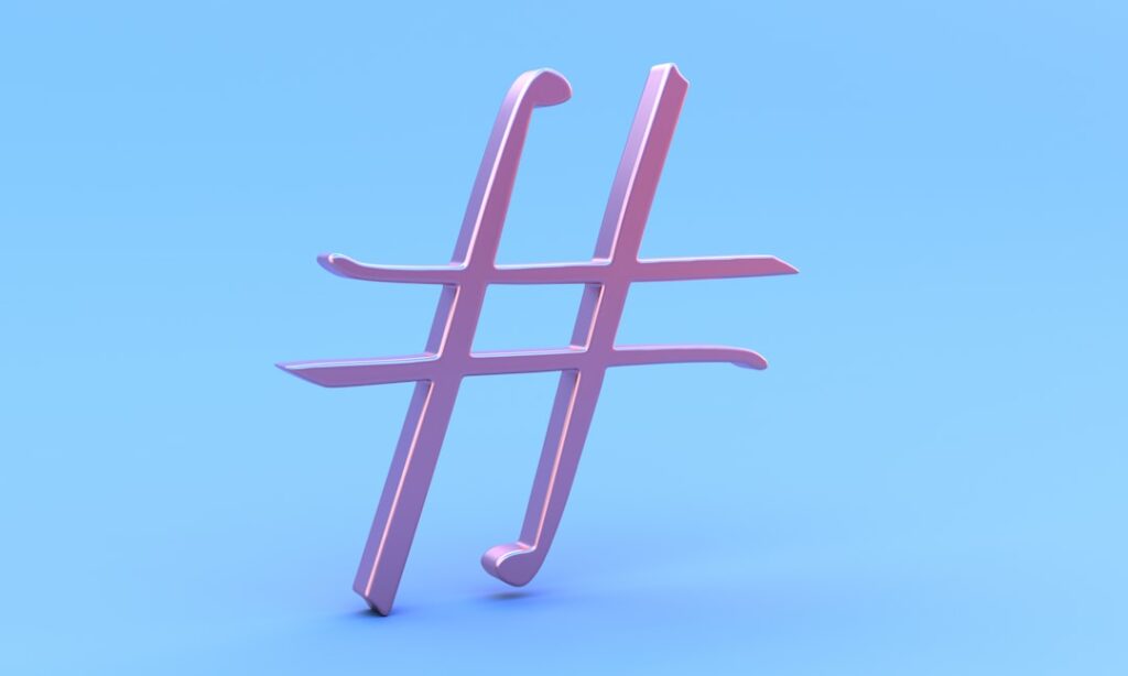 The image features a large, glossy pink hashtag symbol standing upright against a smooth, light blue background.