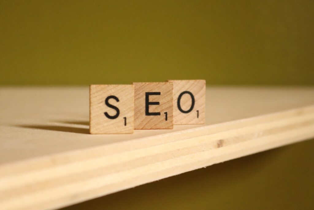 The image-2 product shows three wooden Scrabble tiles, labeled "S", "E", and "O", placed side by side on a light wooden shelf with a plain olive green background.
