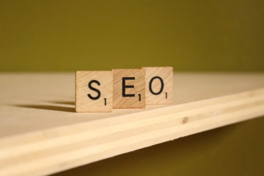 The image-2 product shows three wooden Scrabble tiles, labeled "S", "E", and "O", placed side by side on a light wooden shelf with a plain olive green background.