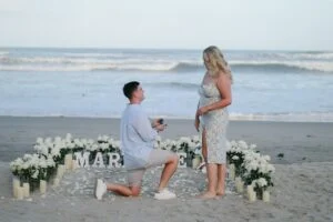 In image-4, a man proposes on a sandy beach with an open ring box, surrounded by white flowers, candles, and large white "MARRY ME" letters, while ocean waves roll in the background.