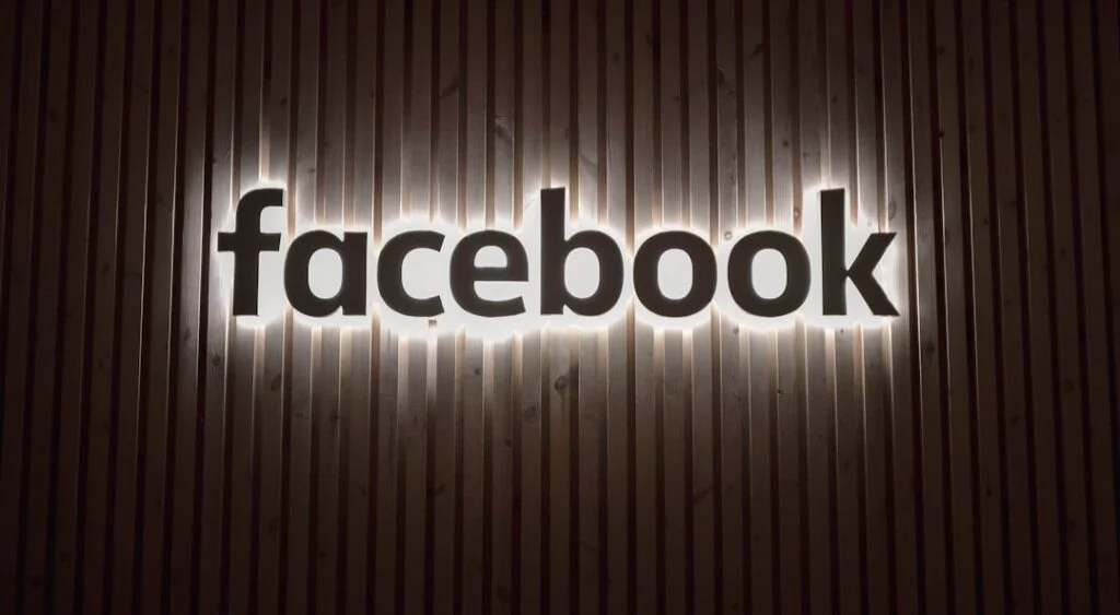 The product "image-6" displays the illuminated word "facebook" in lowercase on a vertically grooved wooden panel wall, creating a modern and stylish effect.