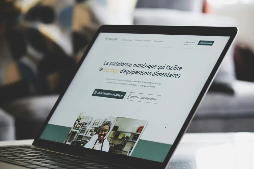 A laptop displays “160920261789521423.jpeg,” which shows a French website focused on sharing food equipment, with a woman pictured below the main text. The screen is in focus, while the background appears blurred.