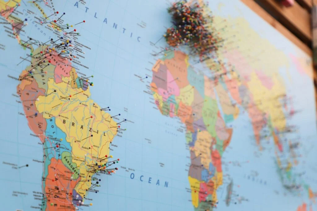 210920261789953416.jpeg features a vibrant world map with numerous colorful pins marking locations across South America, Africa, and Europe. The Atlantic Ocean is prominently labeled at the center of the map, highlighting map pins that indicate visited or significant places.
